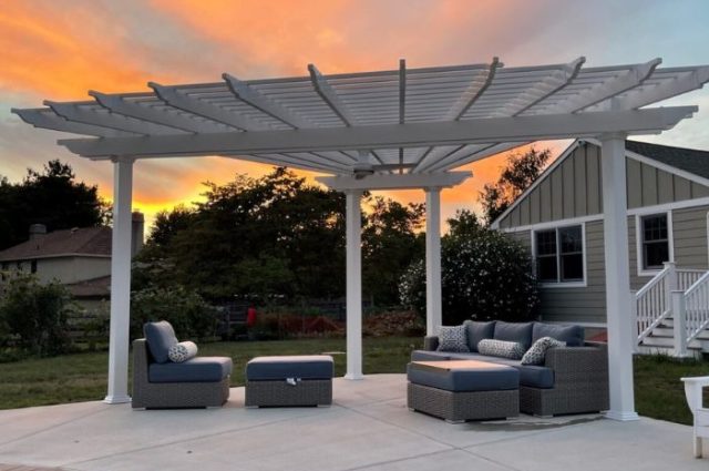 custom detached pergola in vinyl beside a pool and covering a couch and chair with cushions in a backyard