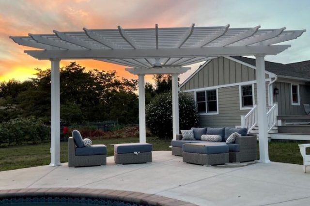 triangle shaped pergola with four posts beside a pool and over a mix of outdoor furniture with cushions