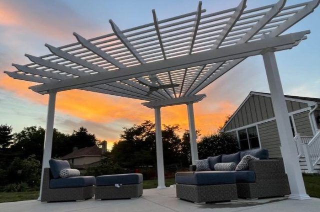 a detached pergola over outdoor chair and couch at sunset beside a pool