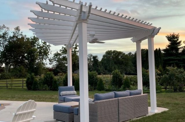 side view of a white vinyl pergola over patio furniture beside a pool area