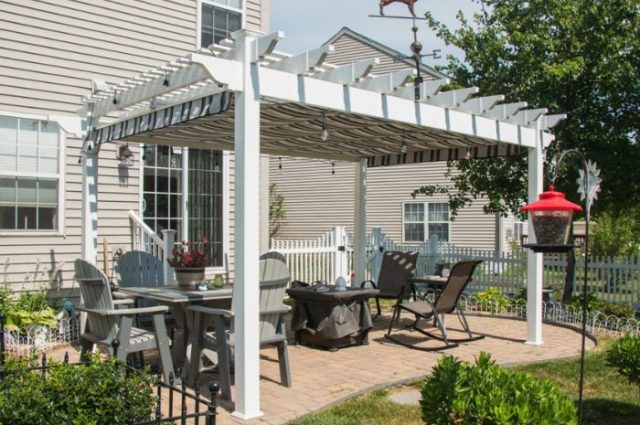 detached white vinyl pergola over a brick patio that has table and chairs underneath
