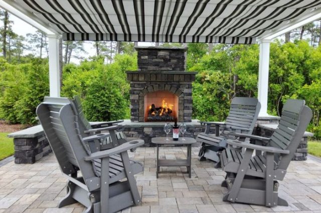 gray polywood rocking chairs under a detached pergola with a canopy and beside a stone fireplace all on a patio