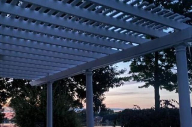 side view of white attached pergola over outdoor seating area during sunset