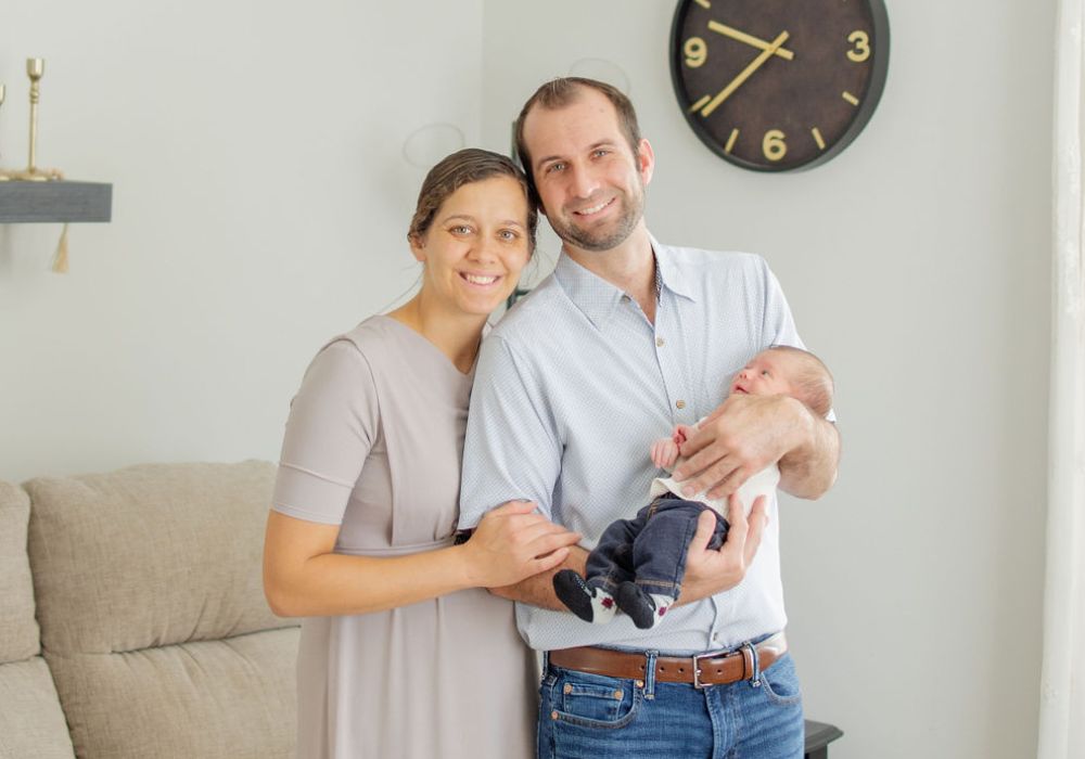 smiling man and woman holding a baby and standing in a living room