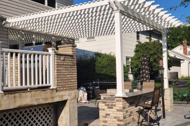 side shot of an pergola attached to a home wtih stone columns around the front posts and over a patio area