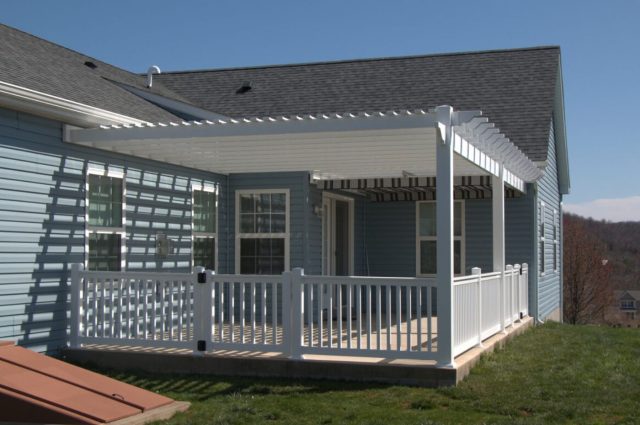 White vinyl pergola attached to blue house with matching railings, creating shaded porch area.