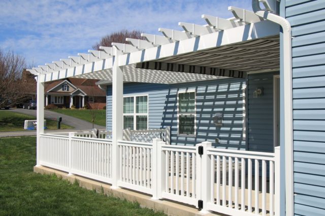 Vinyl pergola with white railings over porch, attached to a light blue house, providing shade and style