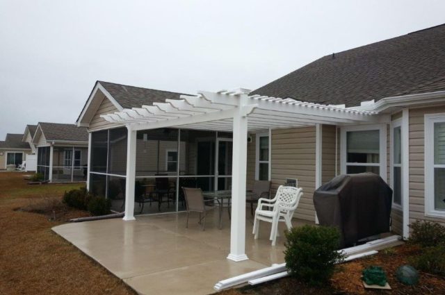 White pergola over patio attached to beige house, with chairs and a covered grill, offering a shaded outdoor area.