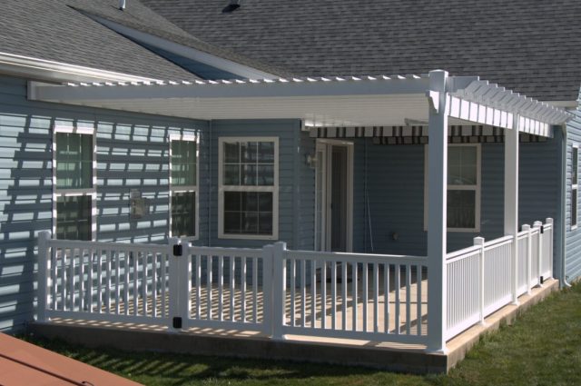 Vinyl pergola kit installed over a deck, attached to a blue house, with white railings for safety and style.