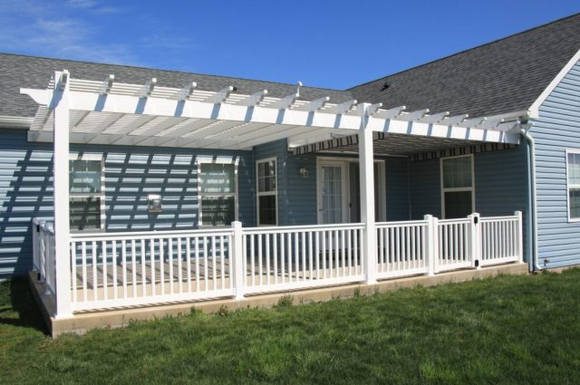 White vinyl pergola placed over a deck, attached to a blue house, offering shade and a stylish outdoor space.