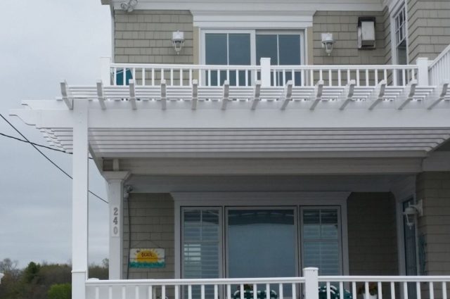 white vinyl pergola attached to the front of the beach condo, providing shade and style to the patio area.