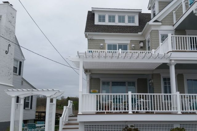 Front view of the beach condo featuring white vinyl pergolas and arbors, with neatly landscaped surroundings and multiple deck levels.