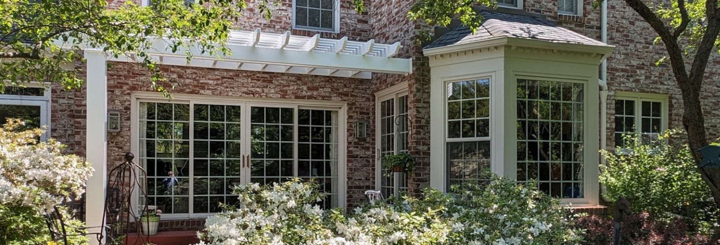 beautiful brick home featuring a white vinyl pergola kit and blooming garden